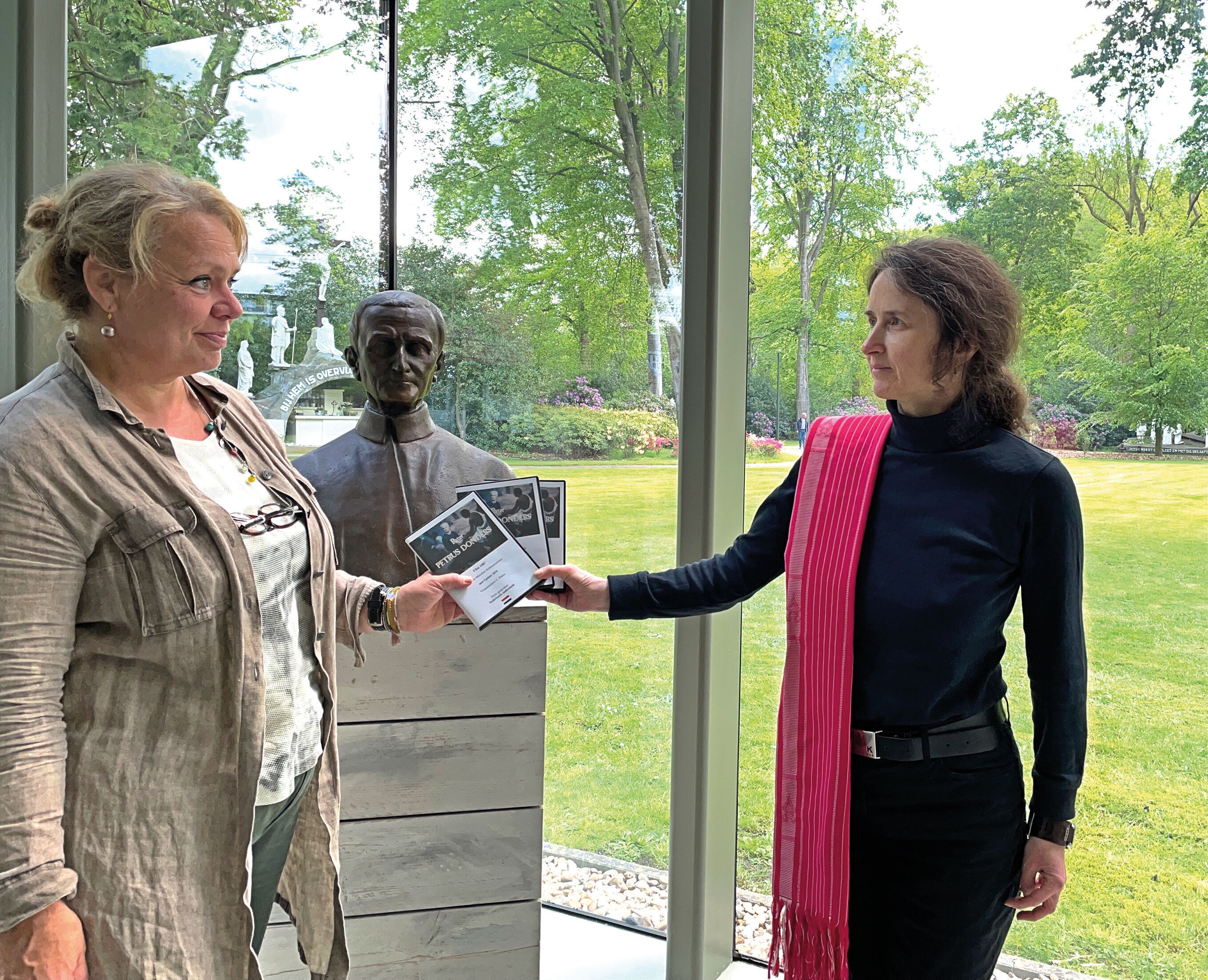 Vicepostulator Claudia Peters (rechts) overhandigt aan Esther Becx, coördinator van het Peerke Donderspaviljoen, exemplaren van een film over Petrus Donders.